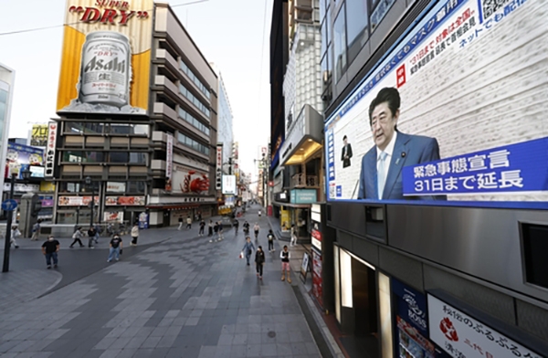 지난 4일 아베 신조(安倍晋三) 일본 총리가 코로나19 긴급사태 연장 방침을 표명하는 장면이 일본 오사카(大阪)에 설치된 대형 모니터에 중계되고 있다. [사진=연합뉴스]