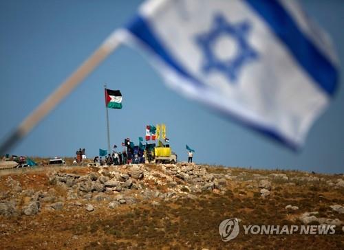 이스라엘 북부 국경에 내걸린 이스라엘 국기 뒤로 레바논에서 레바논 국기와 팔레스타인, 헤즈볼라 깃발을 세우고 반이스라엘 시위를 벌이는 사람들. [사진=AFP/연합뉴스]