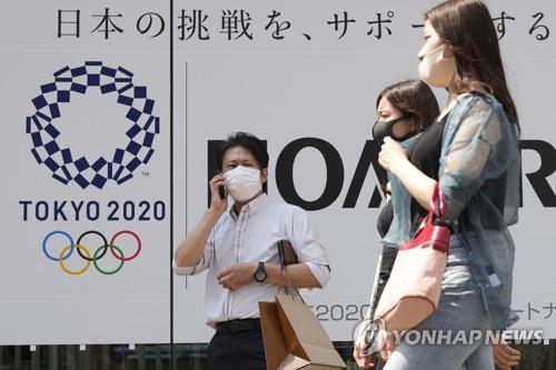 지난달 25일 일본 도쿄도에 설치된 올림픽 홍보물 근처에서 마스크를 쓴 사람들이 이동하고 있다. [도쿄 AP/연합뉴스]