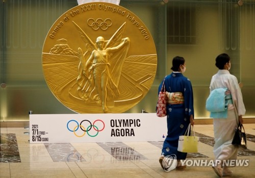 도쿄의 니혼바시 미쓰이 타워에 설치된 대형 올림픽 메달 모형 앞을 전통 복장에 신종 코로나바이러스 감염증(코로나19) 예방 마스크를 쓴 여성들이 걸어가고 있다. [로이터=연합뉴스]