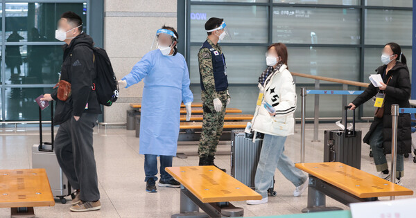 9일 오전 인천국제공항 제1여객터미널에서 중국발 입국자들이 노란 패찰을 목에 걸고 입국장으로 들어서며 방역 관계자의 안내를 받고 있다. [연합뉴스]