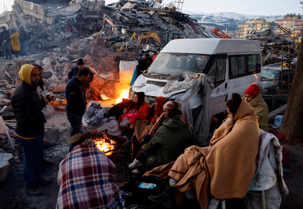 튀르키예 남부 카흐라만마라슈시에서 지진 피해자들이 무너진 건물 잔해 옆에서 모닥불을 피워 몸을 녹이고 있다. [로이터=연합뉴스]